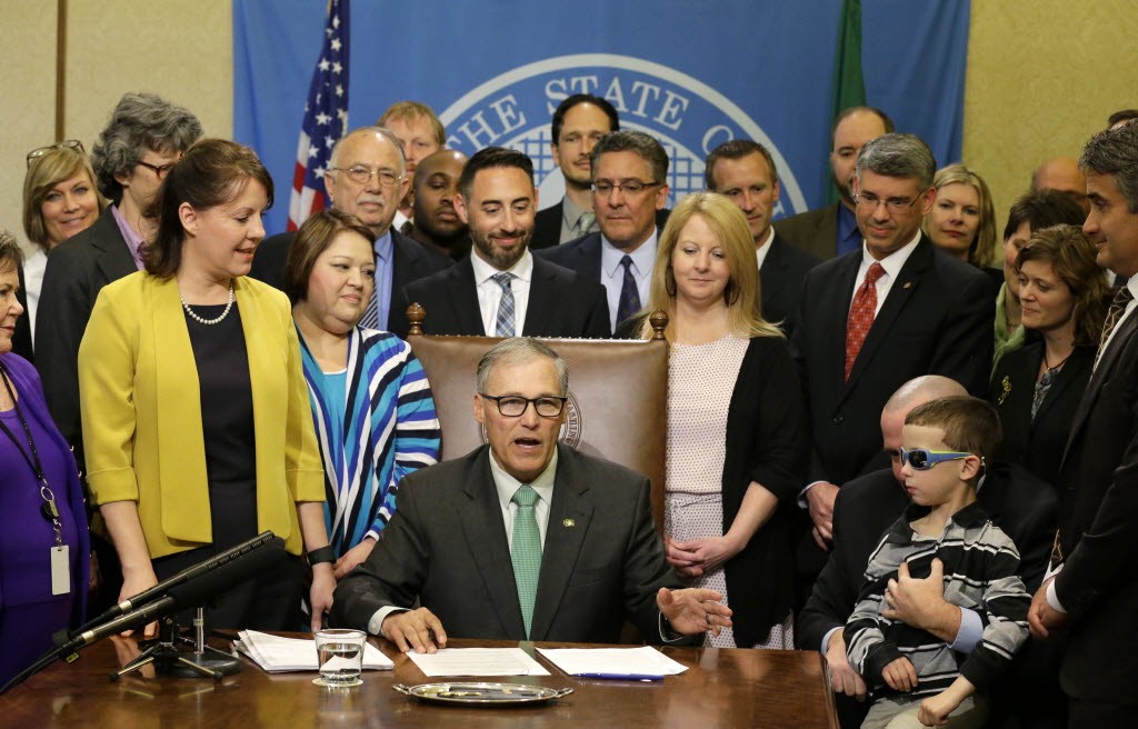A group of lawmakers and supporters stand at the desk of Gov.  Jay Inslee on April 24, when he signed bill overhauling the state's medical marijuana system. 